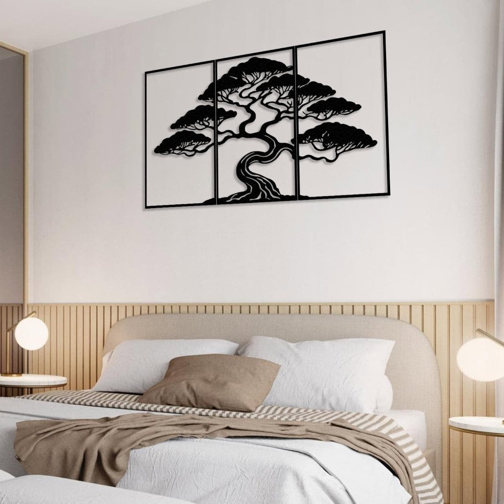 Three-piece black metal wall art featuring a bonsai tree with intricate details, mounted on a light wall above a cozy bed. The bed is styled with white linens, beige accent pillows, and a striped throw blanket, flanked by two round bedside tables with modern globe lamps.