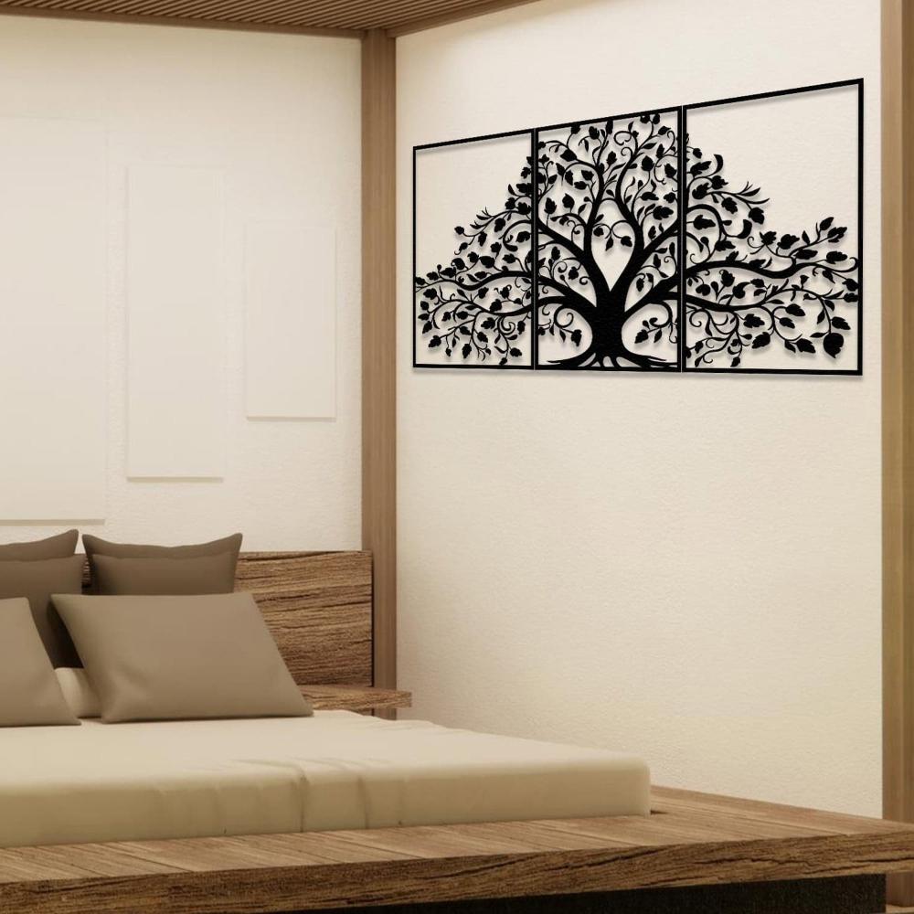 Three-piece black metal wall art featuring a life tree with intricate branches and leaves, mounted on a light wall in a minimalist bedroom. Below the artwork, a wooden platform bed is styled with neutral bedding and accent pillows, complementing the natural decor.