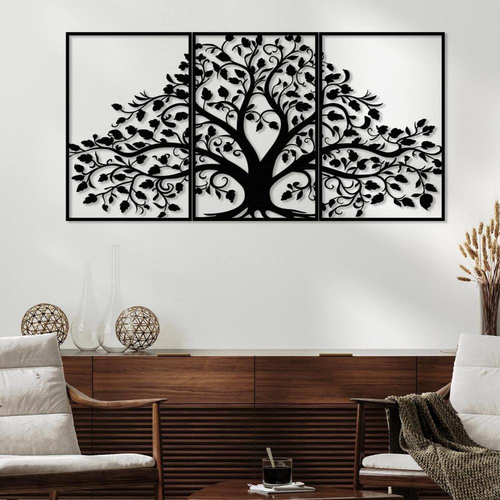 Three-piece black metal wall art featuring a life tree with intricate branches and leaves, mounted on a white wall above a wooden sideboard. The sideboard is adorned with glass vases and wicker ornaments. The room includes two modern cushioned chairs and a small coffee table with a glass of coffee and a textured throw blanket, creating a cozy living space.