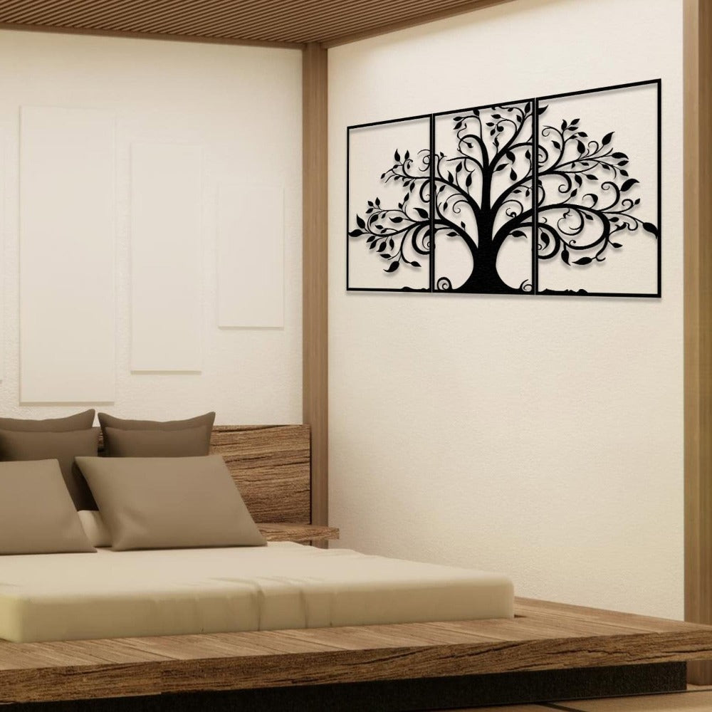 Three-piece black metal wall art featuring a tree with swirling branches and leaves, mounted on a light wall above a wooden bed frame. The bed is styled with neutral-colored bedding and accent pillows, complementing the minimalist and natural decor theme.