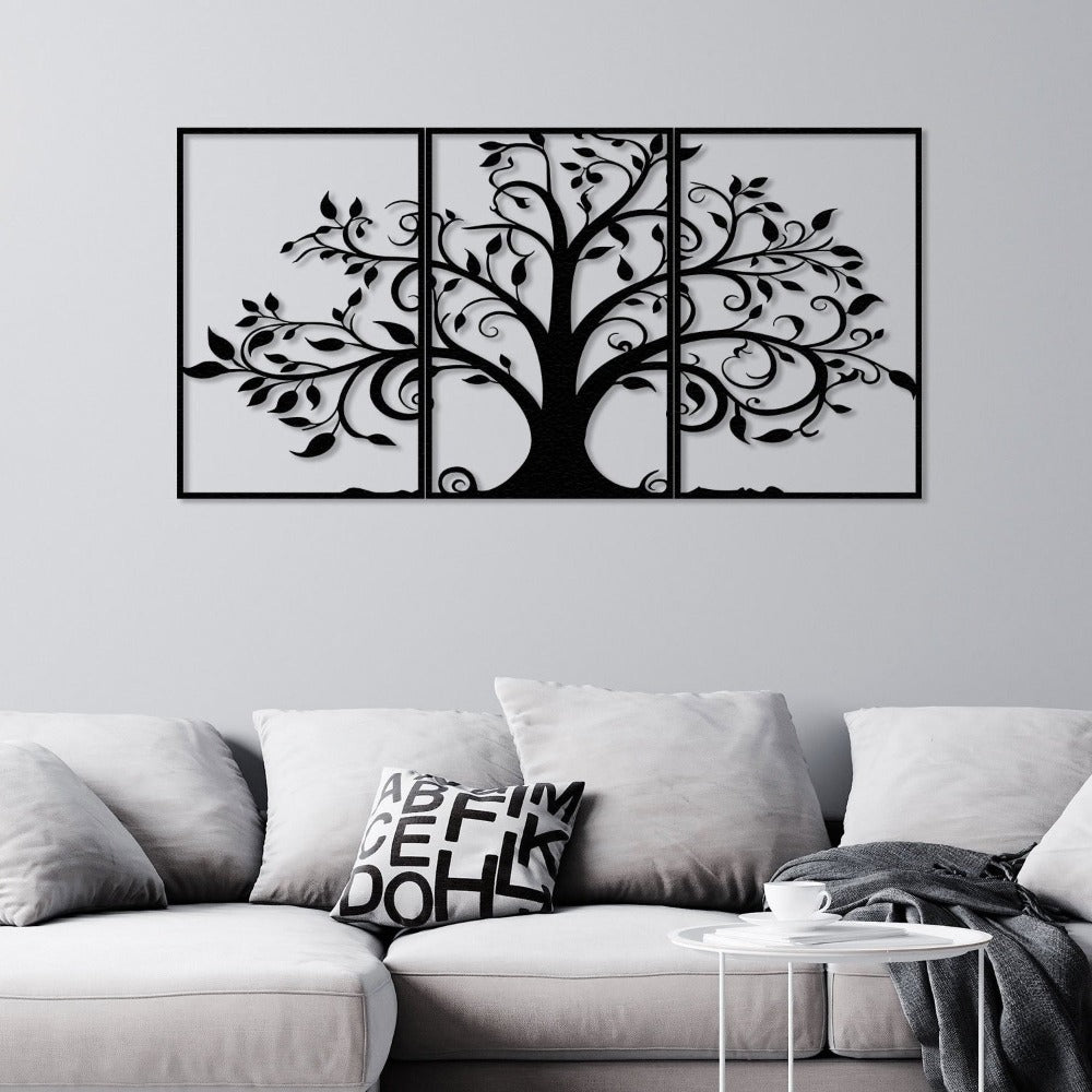 Three-piece black metal wall art featuring a tree with intricate swirling branches and leaves, mounted on a light gray wall above a modern light gray sofa. The sofa is styled with soft cushions, including one with abstract typography, and is accompanied by a small white round side table.