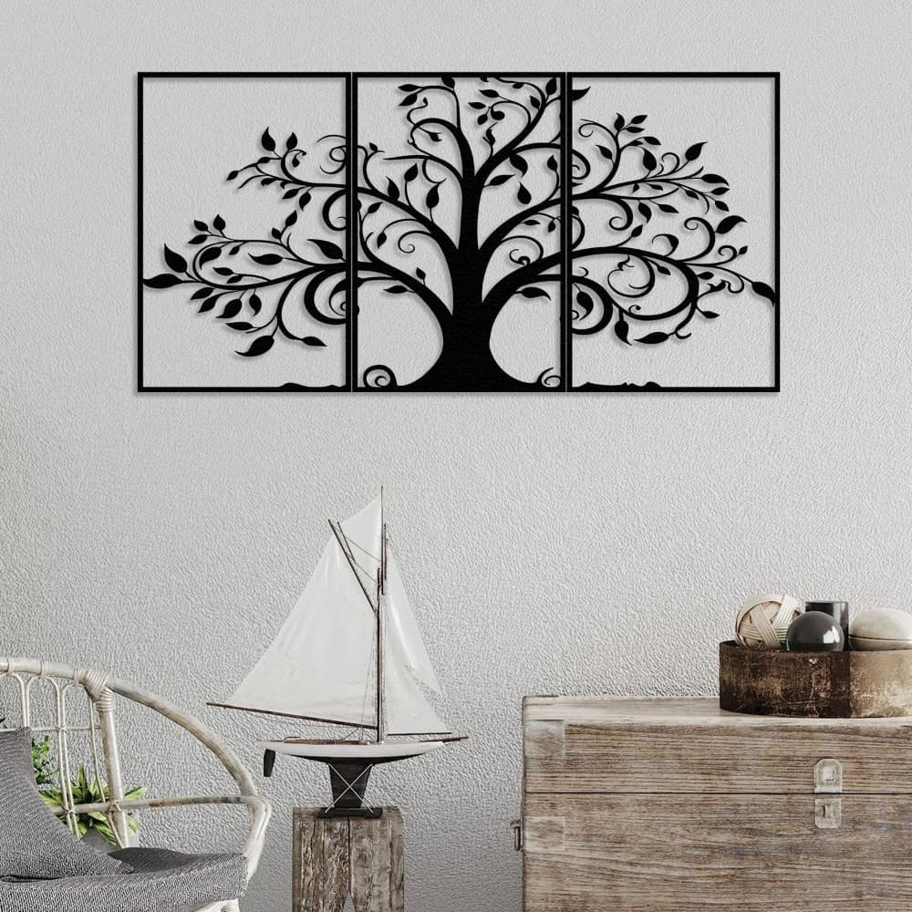 Three-piece black metal wall art featuring an intricate tree design with swirling branches and leaves, mounted on a textured light gray wall. Below, a rustic wooden chest and a wicker chair sit alongside a decorative sailboat and a bowl filled with natural ornaments, creating a coastal-inspired decor.