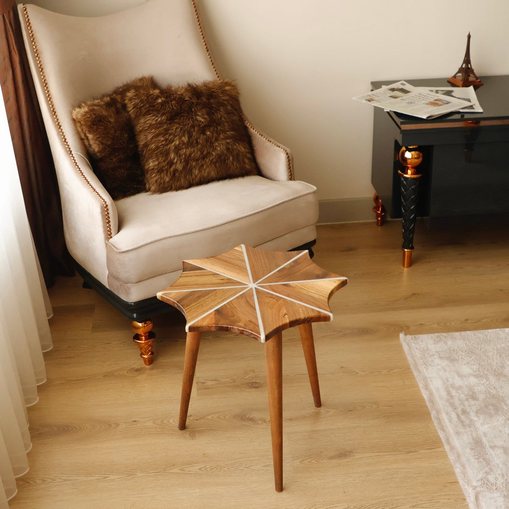 Handcrafted wooden side table with a starburst design, placed in a cozy living room setup. The table complements a beige armchair and adds a modern artistic touch to the interior.