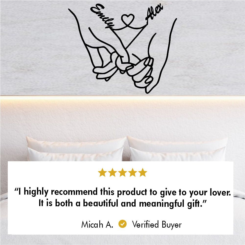 Custom couple's hand-holding metal wall art with "Emily" and "Alex" names connected by a heart symbol, elegantly displayed above a minimalist bed with a glowing headboard. Verified buyer review reads, "I highly recommend this product to give to your lover. It is both a beautiful and meaningful gift."