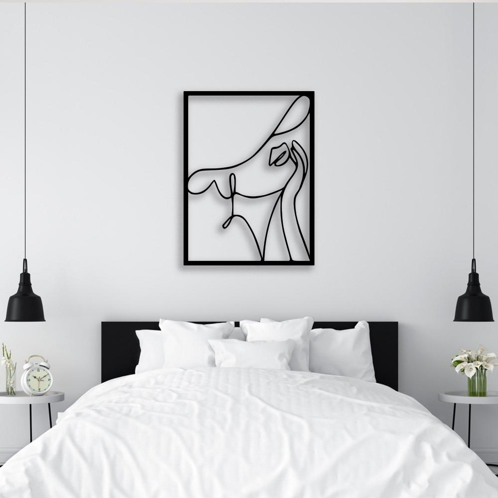 Minimalist black metal wall art depicting an abstract woman with a hat, mounted above a modern bed in a white bedroom.