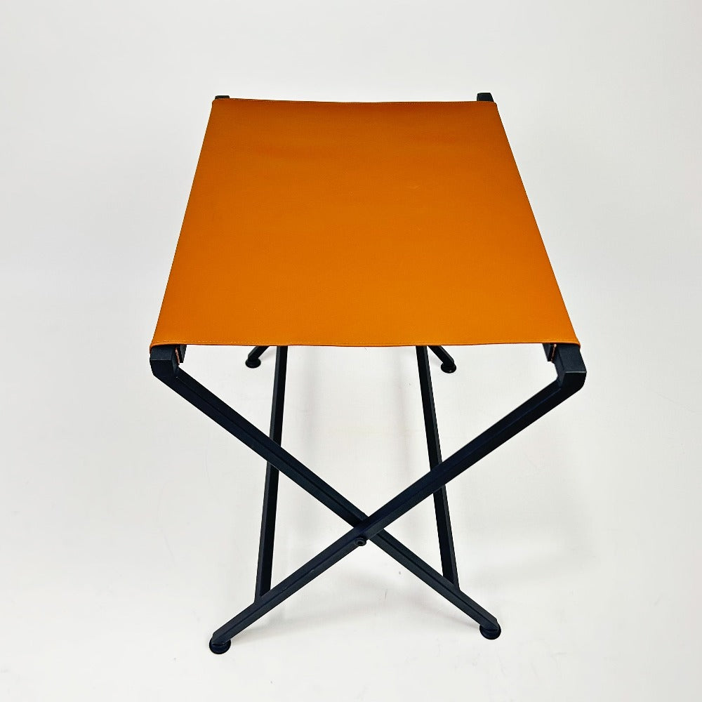 Foldable suitcase rack shown from an alternate angle, with an orange leather top and black metal frame, perfect for compact and stylish storage solutions.