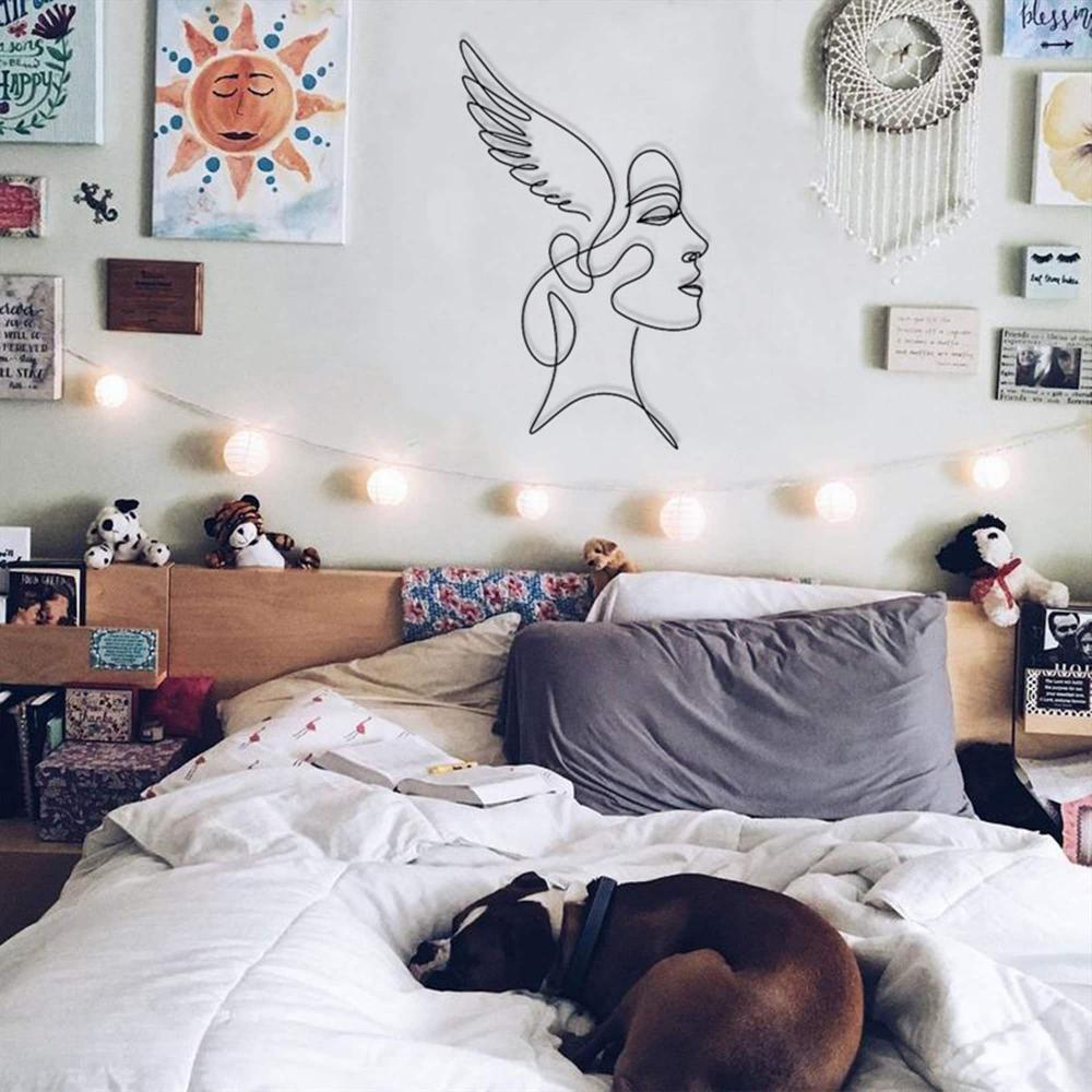 A cozy bedroom with a boho aesthetic, featuring string lights, wall decor, and angelic winged woman wall art above a bed with a sleeping dog.