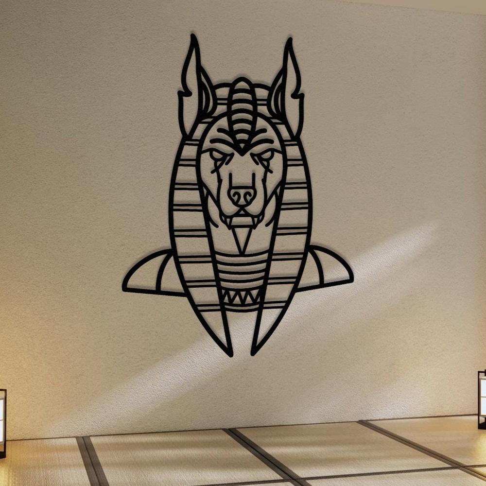 Black metal wall art of Anubis, the ancient Egyptian god, featuring a bold geometric design, mounted on a textured beige wall. The room has a minimalistic aesthetic with tatami-style flooring and soft lighting from lantern-style lamps on both sides.