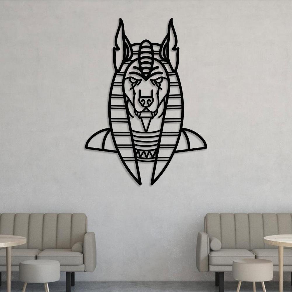 Black metal wall art of Anubis, the ancient Egyptian god, featuring a geometric design, mounted on a plain light gray wall. Below, two beige tufted sofas with rounded backs and matching round tables create a cozy seating area.