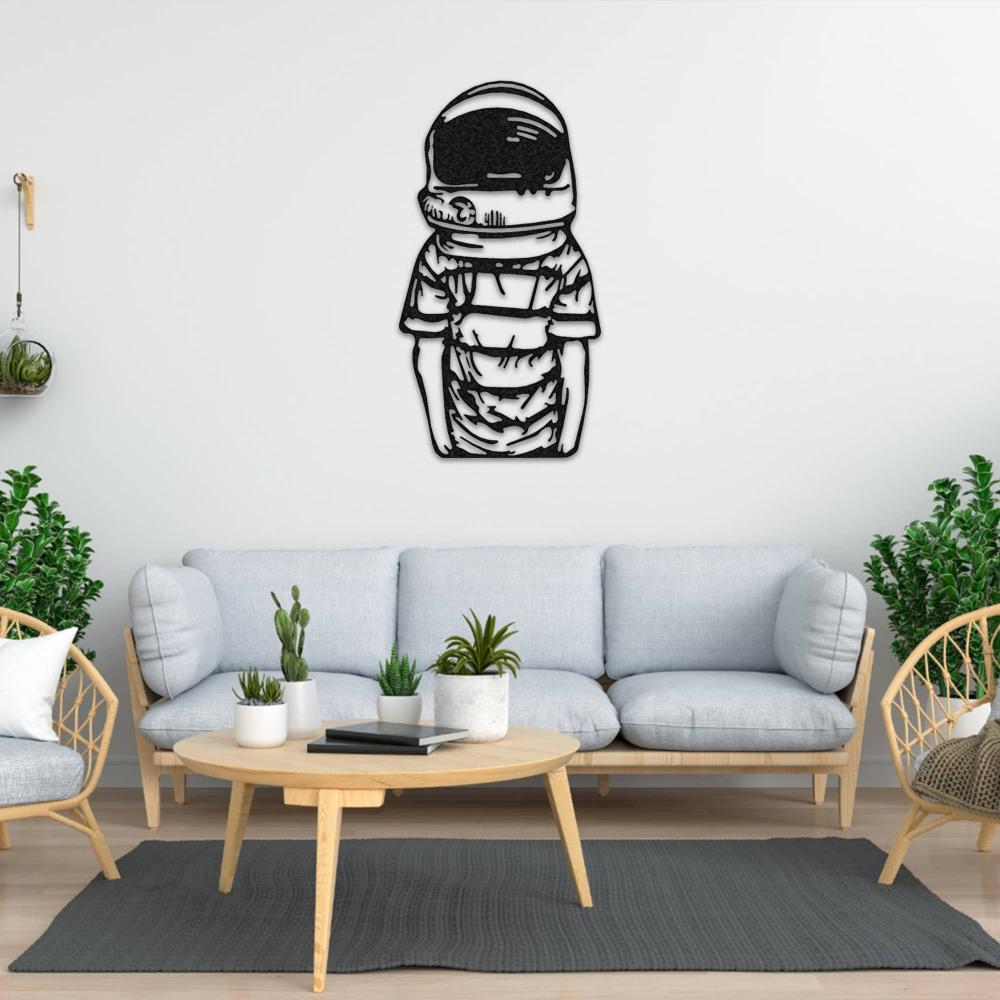 Astronaut metal wall decor featuring a child in a spacesuit, mounted on a light wall in a cozy living room with a light gray sofa, wooden furniture, green plants, and minimalist decor.