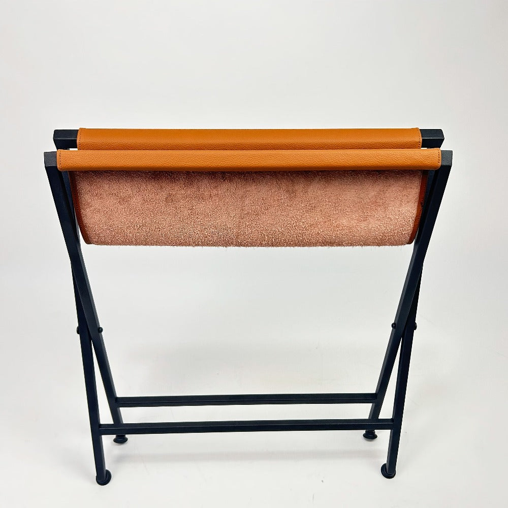 Back view of a foldable suitcase rack, showcasing the orange leather top rolled down and the robust black metal frame