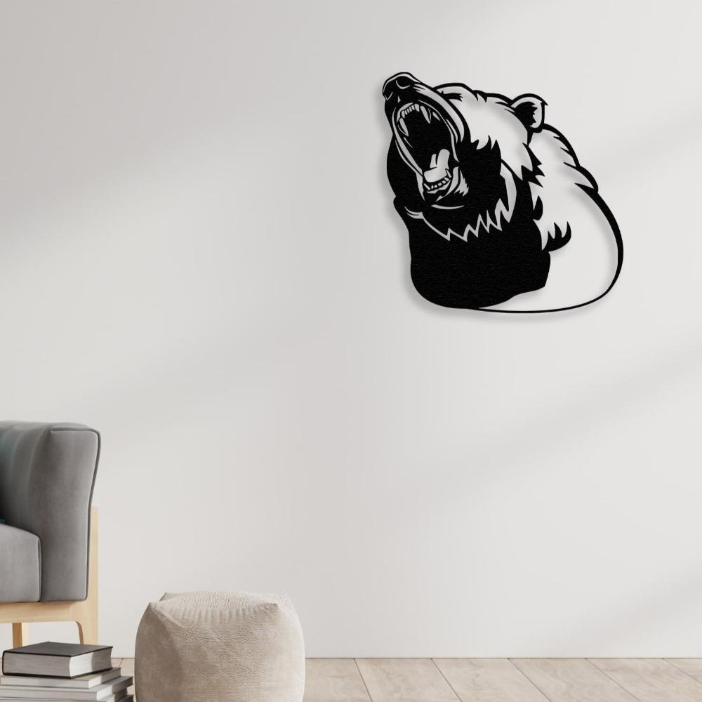 Black metal bear silhouette wall art showcasing a roaring bear head, mounted on a clean white wall in a modern living room with a grey armchair, a beige pouf, and a stack of books on a wooden floor.
