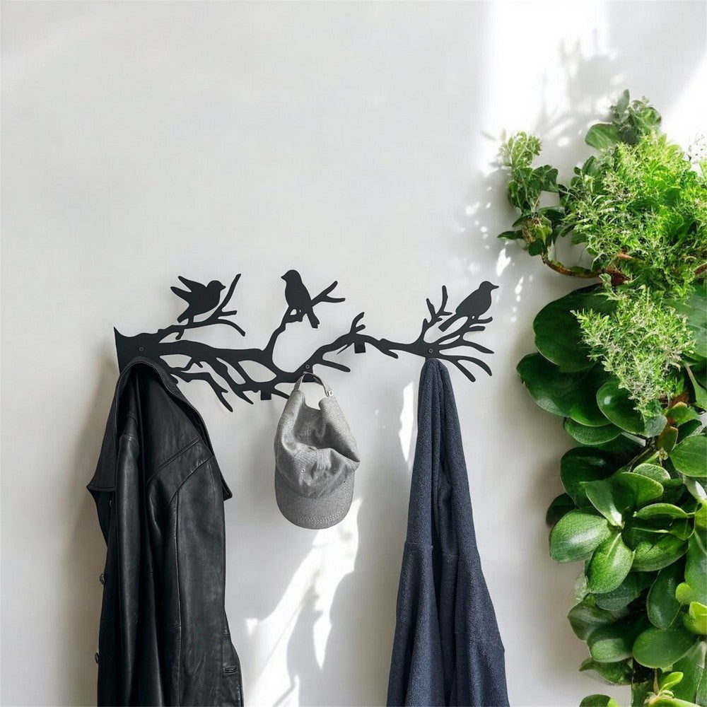 A black metal wall-mounted coat rack with bird silhouettes perched on branches. The rack holds a black leather jacket, a grey cap, and a blue scarf, creating a stylish and functional entryway decor. A green plant next to the rack adds a fresh, natural element to the scene.