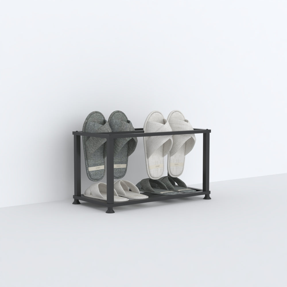 A black angled slipper holder holding two pairs of slippers, one gray and the other mint-green, displayed in a clean, minimalist style against a white backdrop