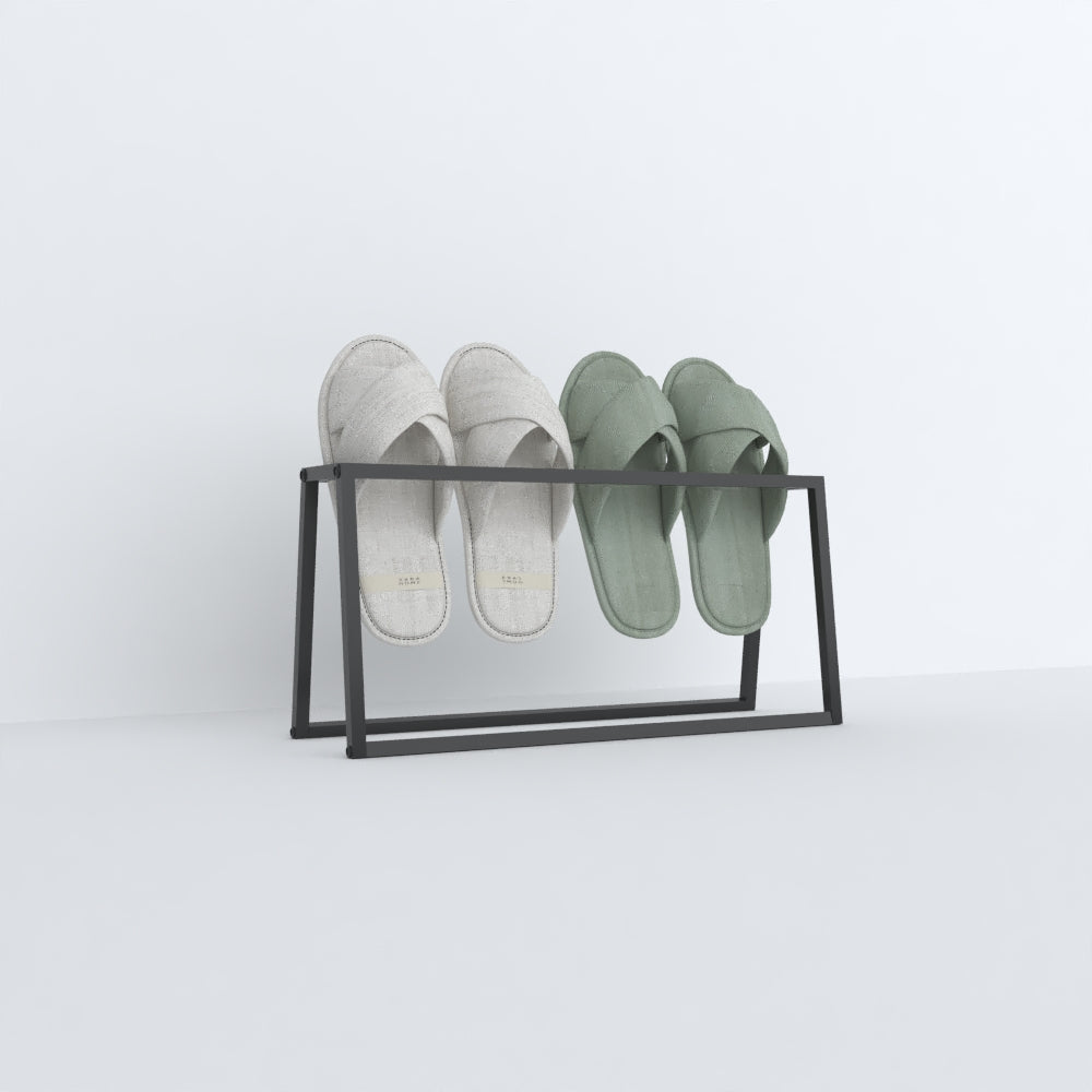 A black angled slipper holder holding two pairs of slippers, one gray and the other mint-green, displayed in a clean, minimalist style against a white backdrop