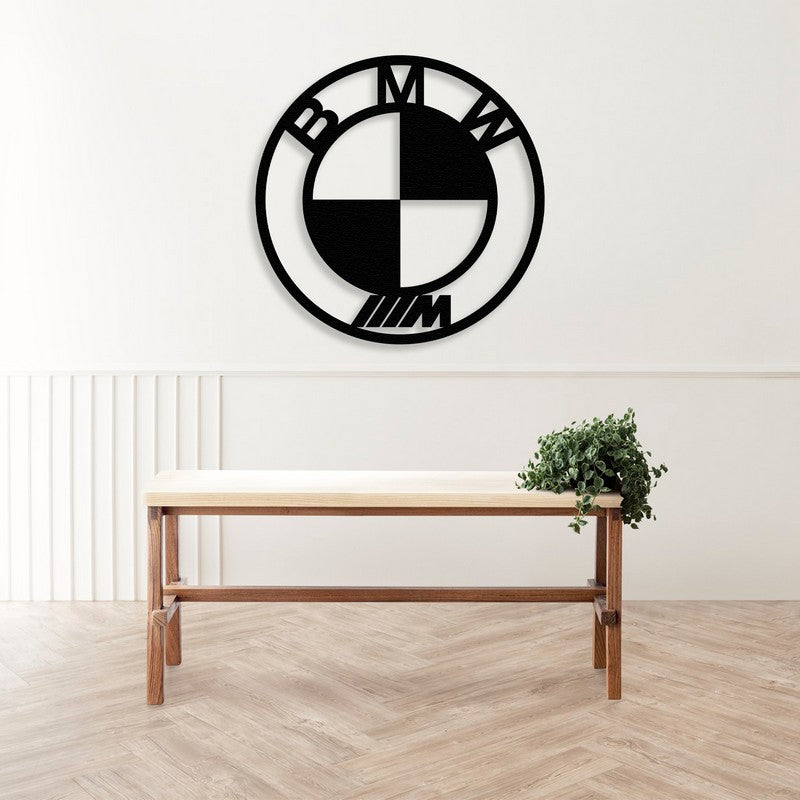 Black BMW-inspired metal car logo wall art mounted above a cozy cream-colored sofa with decorative pillows in a modern living room setup.