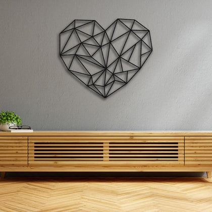 Minimalist geometric heart-shaped metal wall art in black, mounted on a light gray wall above a modern wooden console, with a small plant and a pair of glasses for decor.