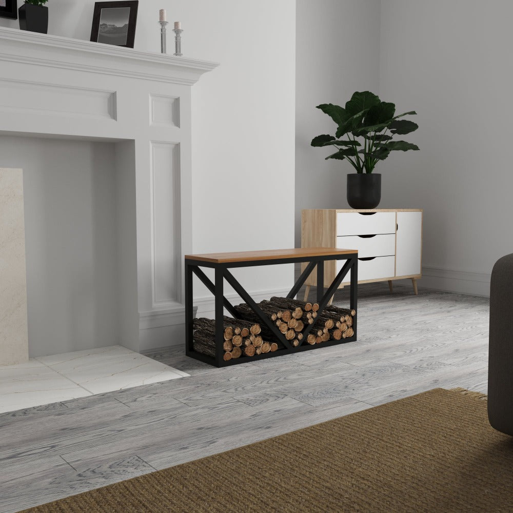 A black metal log holder with a wooden bench placed in a cozy living room. The bench's frame has a diagonal design, and the natural wood top adds a rustic charm.