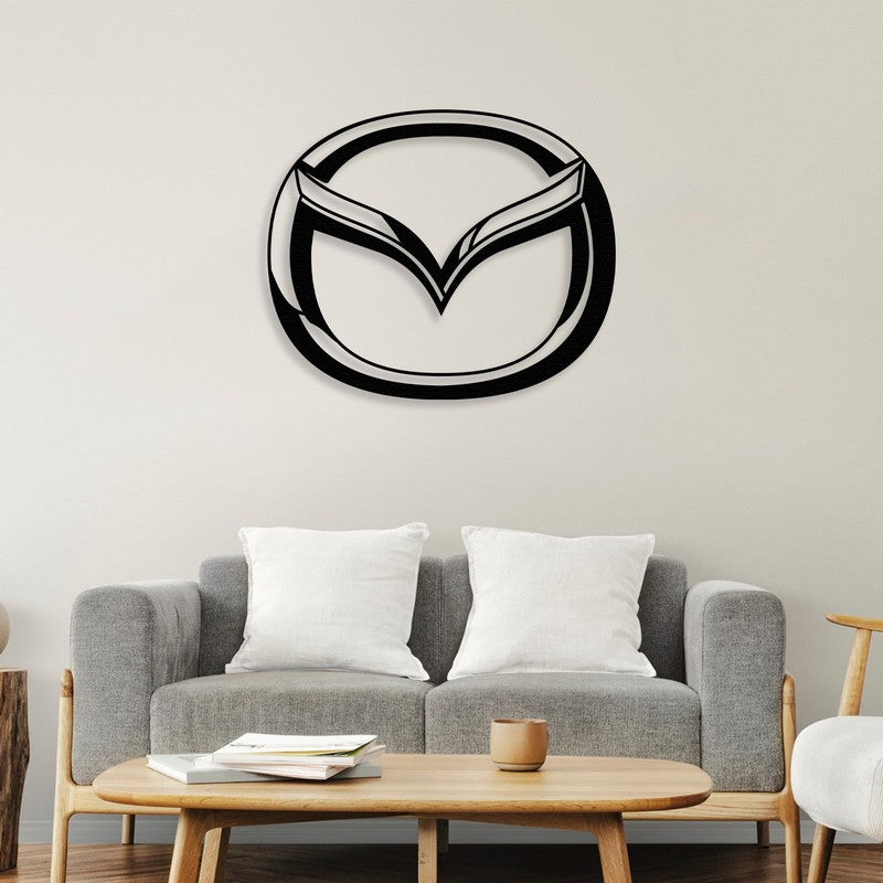 A modern Mazda-inspired black metal wall art elegantly mounted above a minimalist gray sofa with white cushions, accompanied by a sleek wooden coffee table holding books and a ceramic cup, creating a cozy yet stylish living room atmosphere.