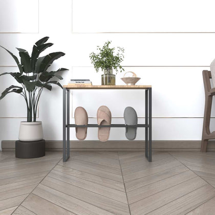 A black metal slipper rack with a wooden top, holding slippers on the lower bars and decorated with books and plants, placed in a sophisticated interior setting.
