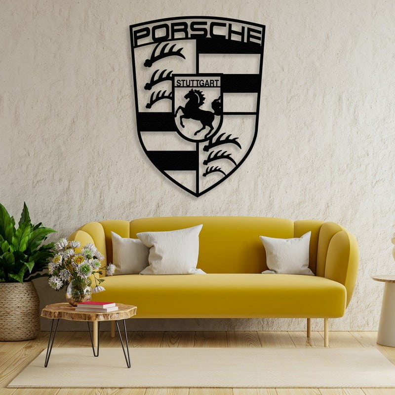 Black metal Porsche emblem car logo wall art featuring intricate designs, mounted on a textured beige wall above a vibrant yellow sofa. The room is adorned with a rustic wooden coffee table, fresh flowers, and indoor plants, creating a cozy yet stylish ambiance.