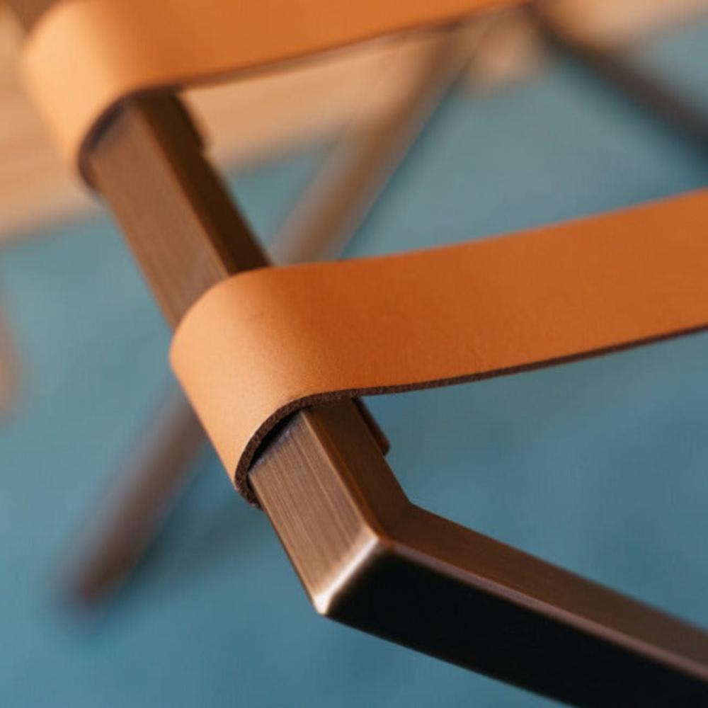 Close up view of a foldable metal luggage rack with black straps positioned near an orange sofa on polished dark flooring