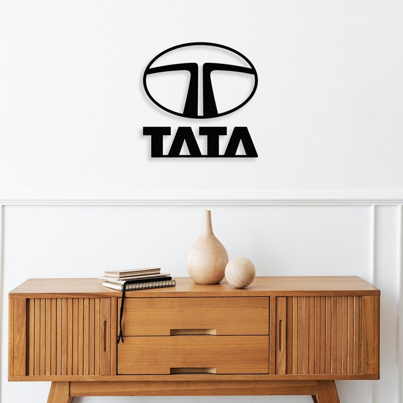 Black metal Tata car logo wall art mounted above a mid-century modern wooden console table featuring clean lines and minimalist design. The console is adorned with wooden vases and stacked books, adding a natural and sophisticated touch to the decor.