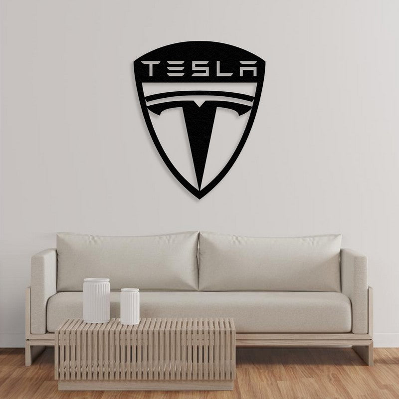 A modern Tesla-inspired black metal car logo wall art design mounted on a plain white wall above a sleek beige sofa with a minimalist wooden coffee table in the foreground.