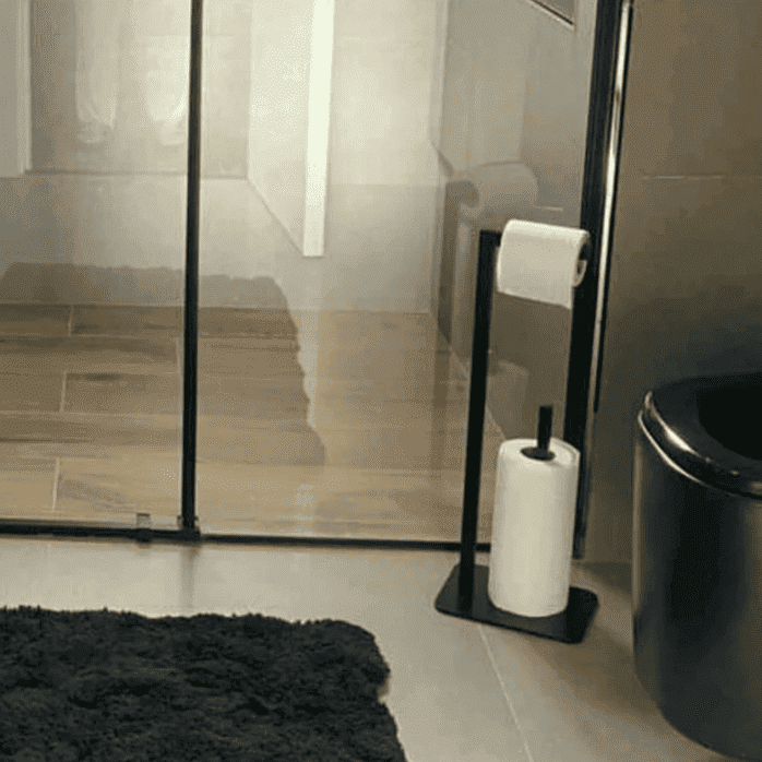 A bathroom setup featuring a black toilet paper holder stand near a glass shower door, complemented by a plush dark rug and elegant interiors.