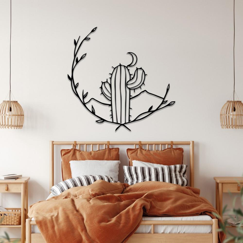 Black metal cactus wall art with a crescent moon and vines, mounted on a white wall above a wooden bed frame. The bed is styled with rust-colored bedding, striped cushions, and two rattan pendant lamps, creating a cozy boho-themed bedroom.