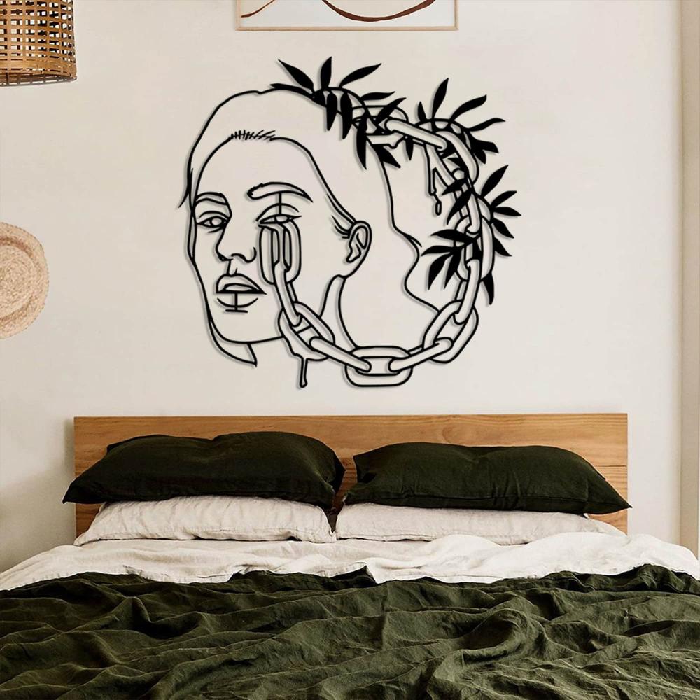 A cozy bedroom with black metal wall art of a woman's face entangled with chains and leaves, mounted above a wooden bed with dark green bedding.