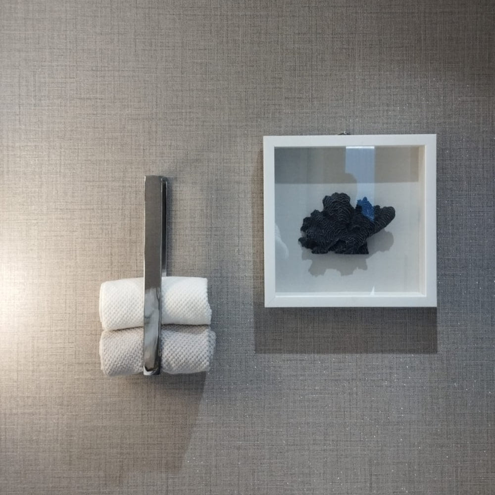 A close-up of a chrome towel holder holding rolled towels, placed next to a framed abstract black and white wall art