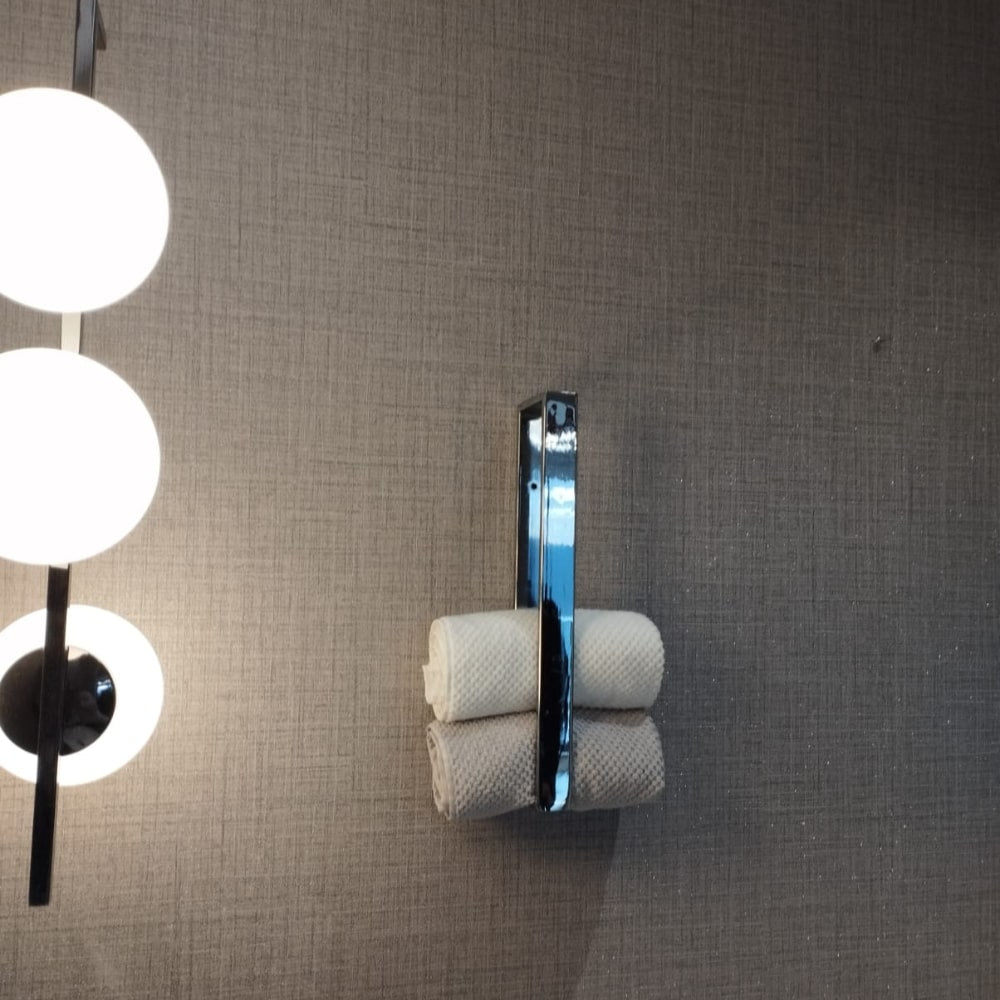 A corner of a modern bathroom with a chrome towel holder, rolled towels, and a woven basket containing toiletries