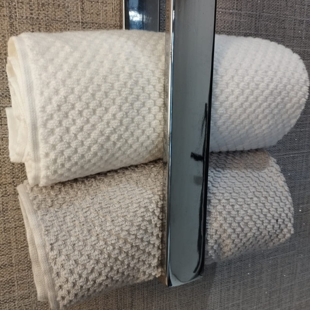 A detailed view of rolled white and beige towels placed neatly in a chrome towel holder against a textured gray wall