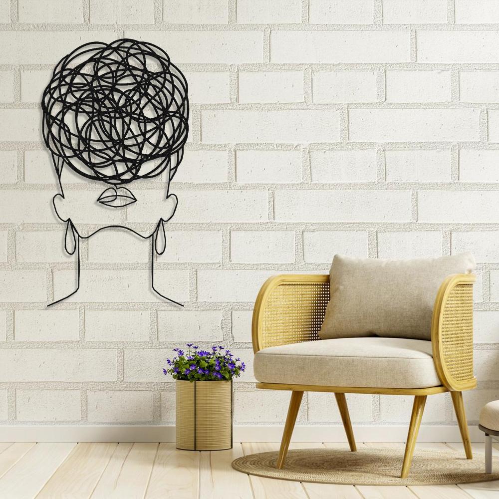 Minimalist black metal wall art of a woman with circular pattern hair, mounted on a vibrant orange wall above a modern lounge chair.