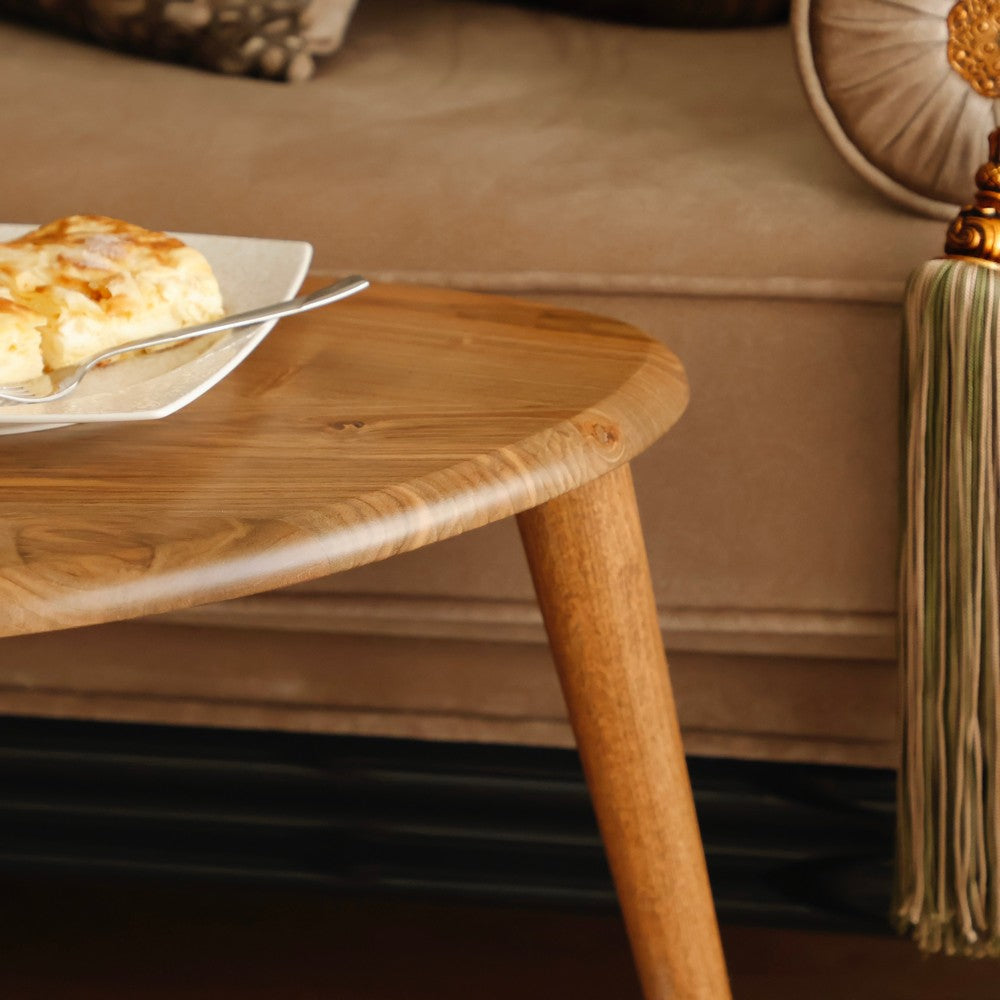 Close-up view of a wooden coffee table with a polished surface, topped with a plate of pastry and a fork, placed near a beige couch with tassel accents.