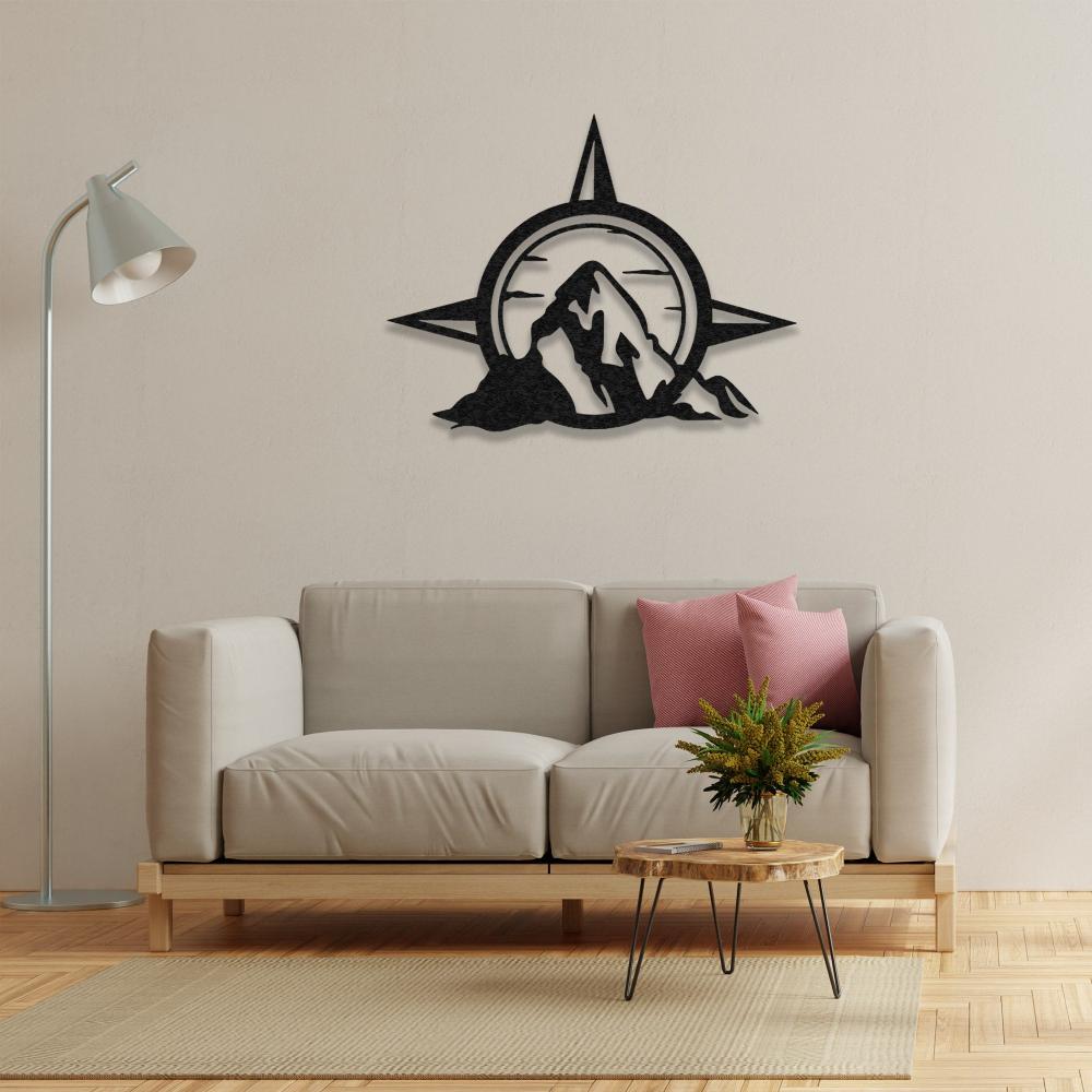 Compass and mountain metal wall art in a warm-toned living room, mounted above a light beige sofa with pink pillows and a wooden table.