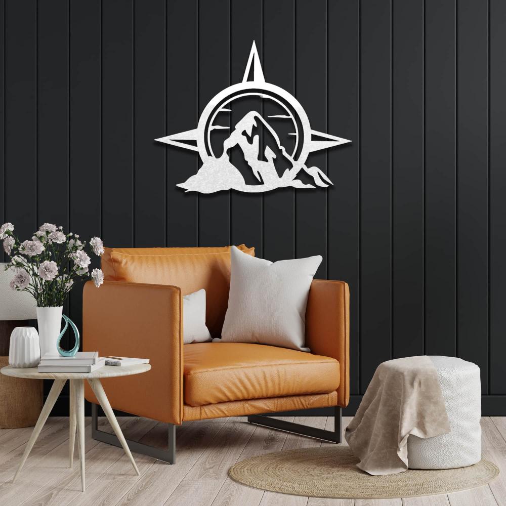 A white version of compass and mountain metal wall art displayed on a dark green wall above an orange accent chair and a small round table.