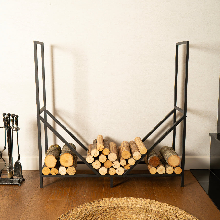 Black metal firewood rack with logs against a white wall