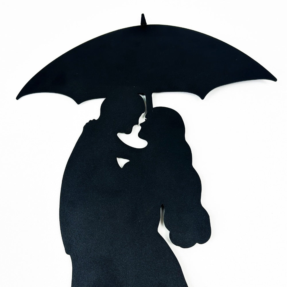 Close-up view of black silhouette metal wall art featuring a romantic couple under an umbrella, highlighting intricate design details on a white background.
