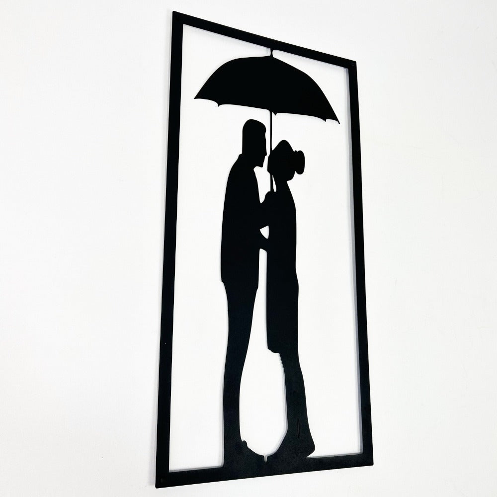 Angled view of a black metal wall art piece featuring a couple standing under an umbrella, emphasizing the clean and elegant design.