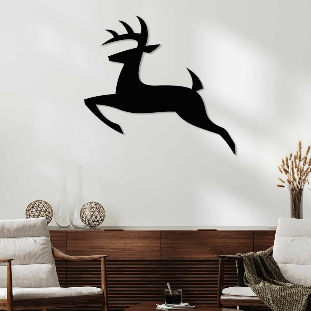 Black silhouette metal wall art of a deer in a leaping pose, mounted on a white wall above a wooden sideboard with decorative glass and wicker accents, flanked by two armchairs.