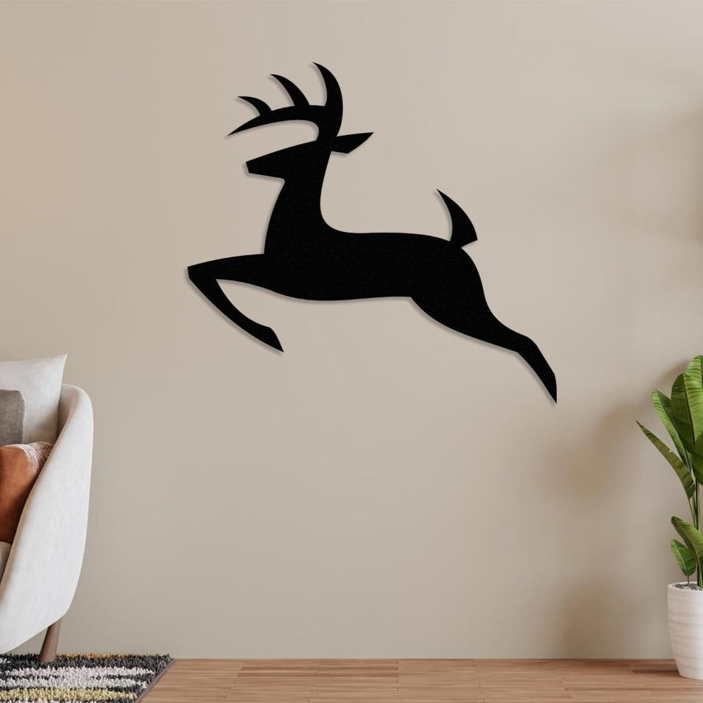 Black silhouette deer metal wall decor mounted on a neutral beige wall, complemented by a cozy armchair with cushions on the left and a green potted plant on the right, creating a modern minimalist aesthetic.