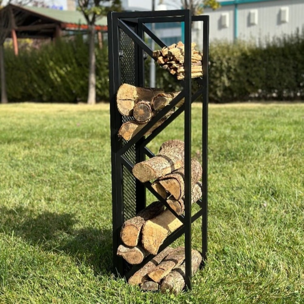 A sleek black metal firewood holder with diagonal shelves and a mesh backing, placed outdoors on a grassy lawn, holding neatly stacked firewood and kindling.