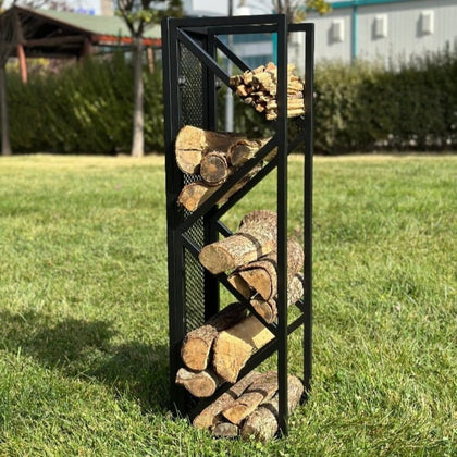 A sleek black metal firewood holder with diagonal shelves and a mesh backing, placed indoors next to a fireplace, holding neatly stacked firewood and kindling.