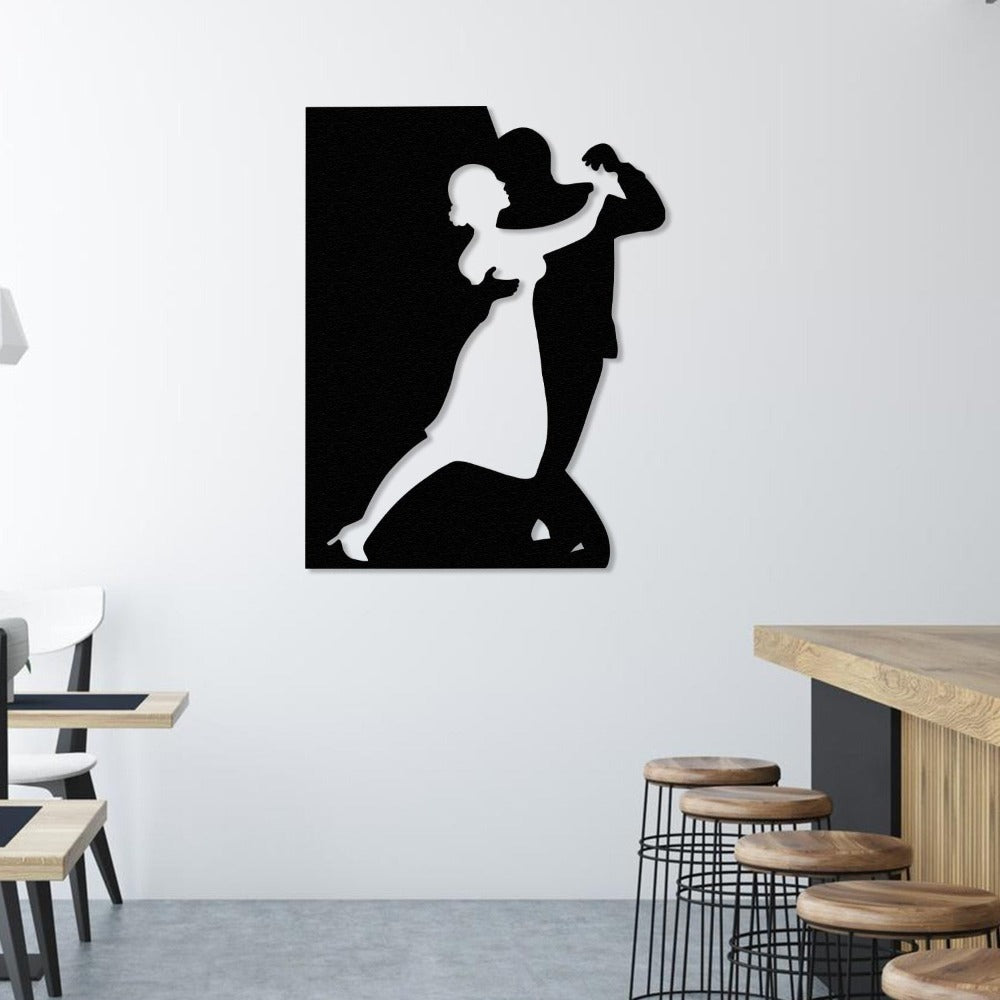 A black metal wall art depicting a couple dancing, displayed on a white wall in a modern dining area with wooden bar stools