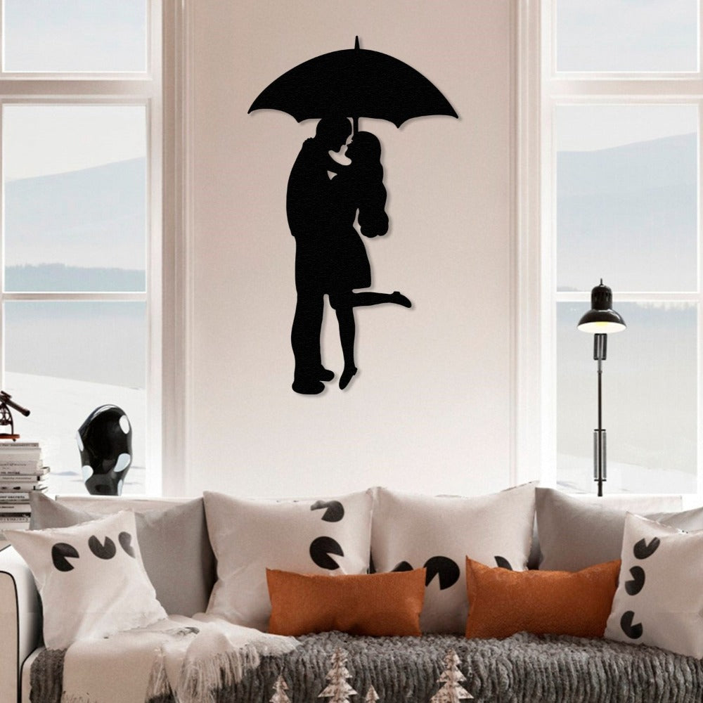 Black metal wall art of a couple under an umbrella, mounted on a white wall above a cozy couch adorned with patterned pillows and orange accents, creating a romantic living room atmosphere.