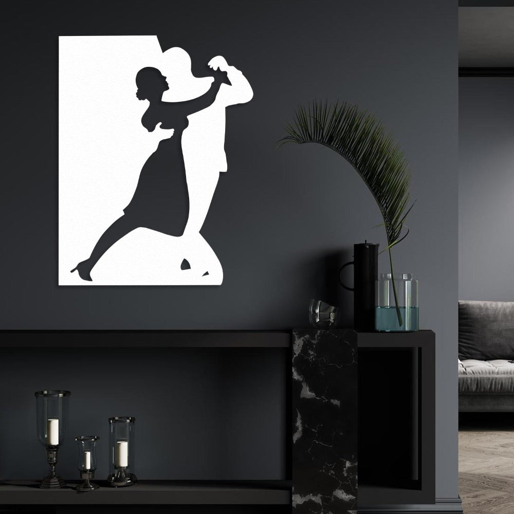 A white metal wall art of a dancing couple, mounted on a dark accent wall, styled with modern decor, including a green plant and sleek candle holders