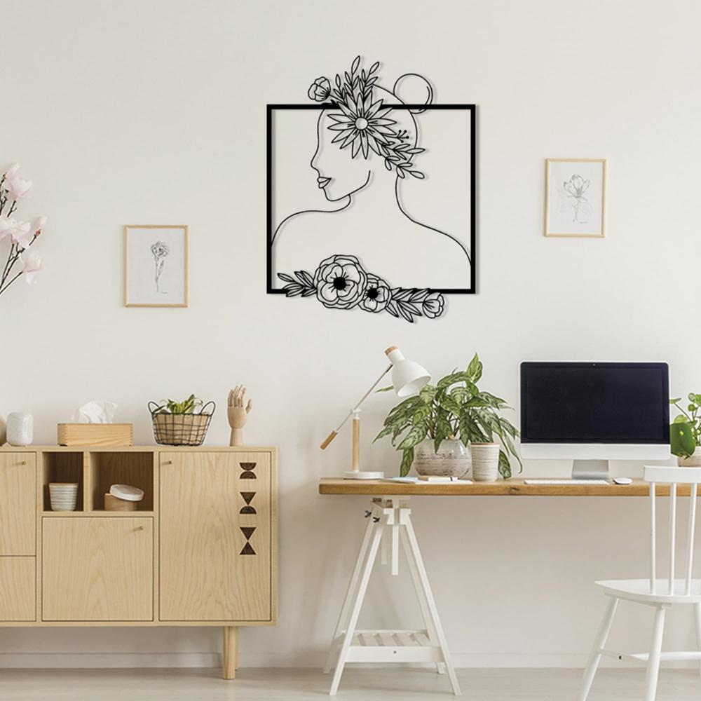 Wall art of a woman with floral accents, showcasing delicate details, mounted in a bright workspace featuring wooden furniture, plants, and minimalistic design elements.