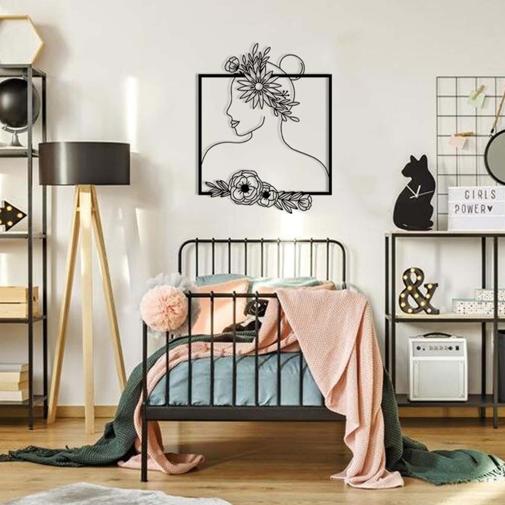 A black floral-themed wall art depicting a woman's silhouette adorned with a flower crown and floral elements at the base, mounted above a black metal bed with soft, colorful bedding in a cozy bedroom setting.